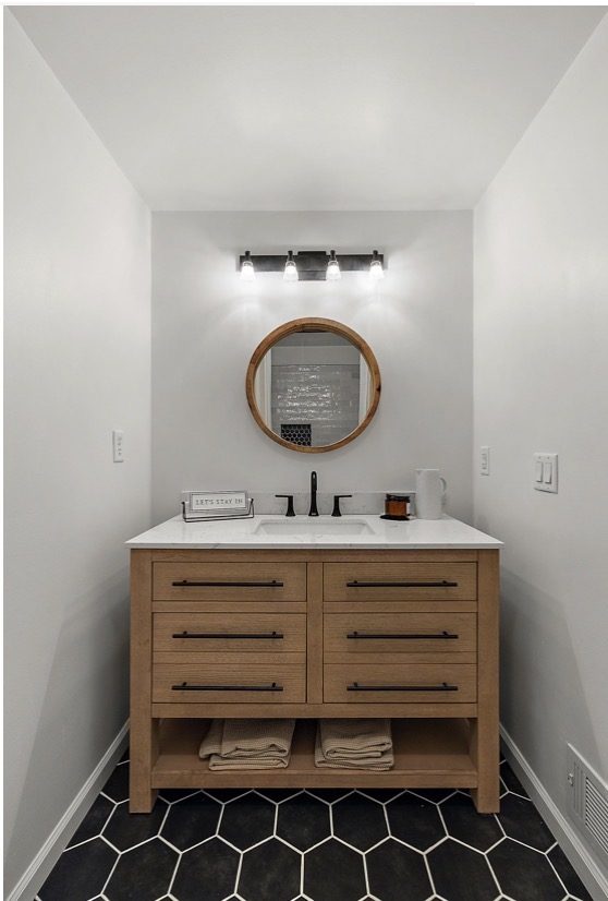 Bathroom remodel with wood vanity, round mirror, and black fixtures — Downriver Michigan